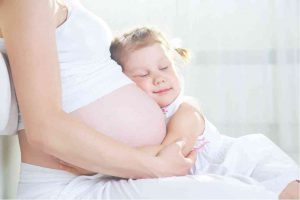 ילדה מחבקת את בטן אמא כשעומד להיוולד לה אח