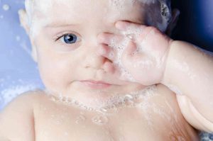 תינוק באמבטיה של קצף משפשף עיניים