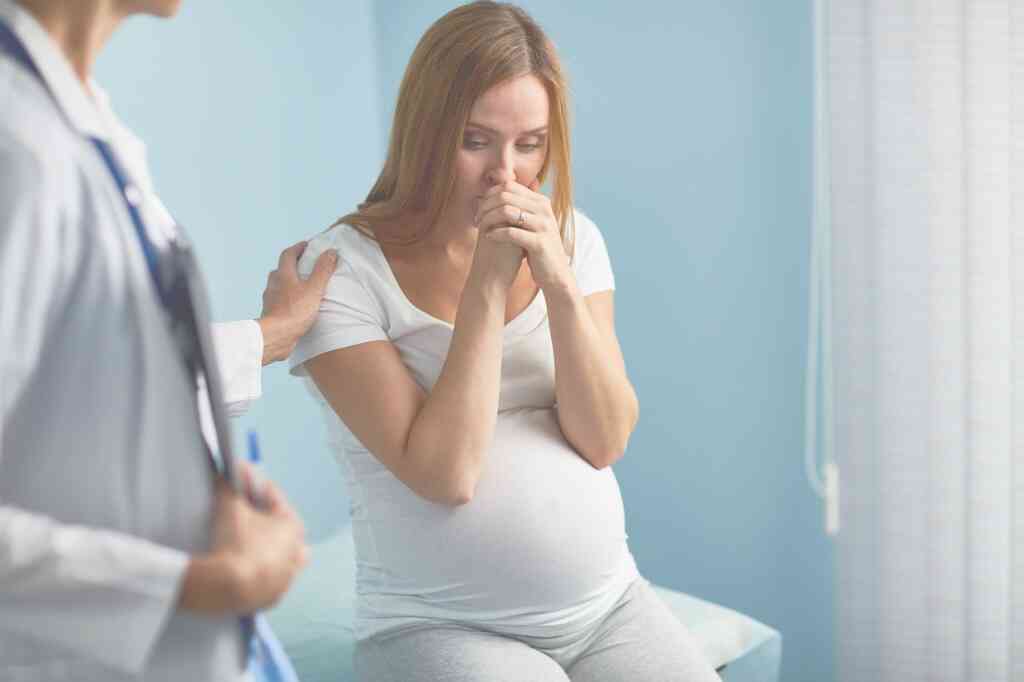 אמא בהריון יושבת על מיטת רופא עצובה בגלל רשלנות רפואית
